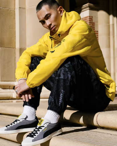 A man sitting on a city step wearing a Puma yellow outfit and matching sneakers