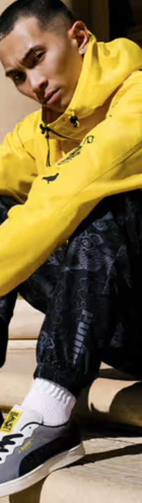 A man sitting on a city step wearing a Puma yellow outfit and matching sneakers