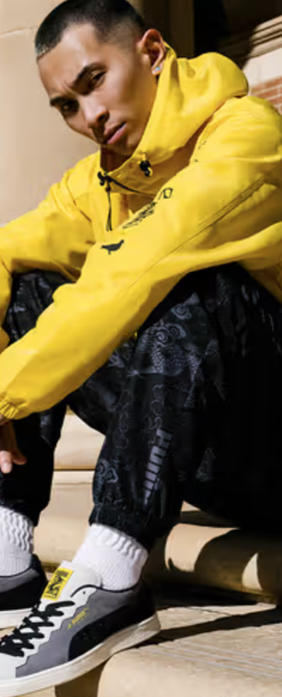 A man sitting on a city step wearing a Puma yellow outfit and matching sneakers