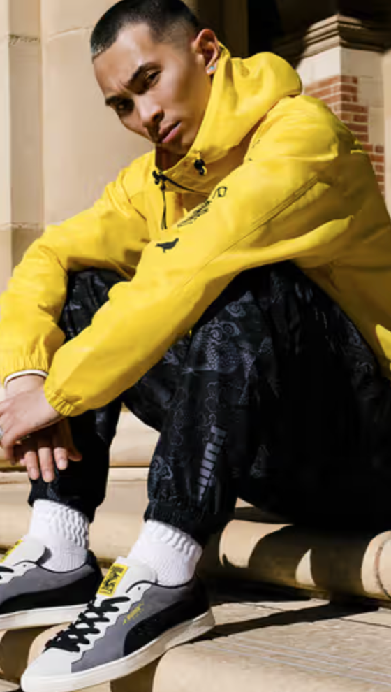 A man sitting on a city step wearing a Puma yellow outfit and matching sneakers