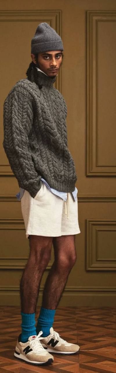 A man in a New Balance outfit with a dark grey fisherman sweater, a matching beanie and blue socks