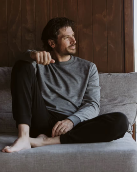 A man sitting in an Icebreaker grey sweatshirt and black pants