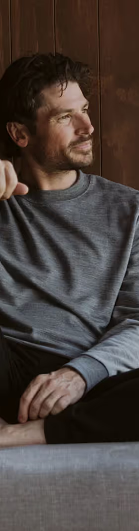 A man sitting in an Icebreaker grey sweatshirt and black pants