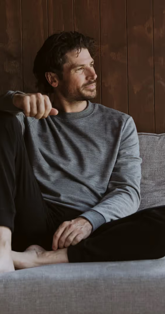 A man sitting in an Icebreaker grey sweatshirt and black pants