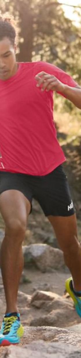 A man running in a Hoka One One outfit with a red shirt, black shorts and colorful sneakers