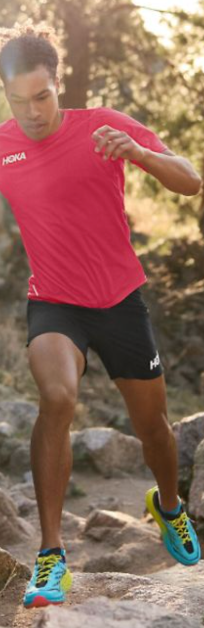 A man running in a Hoka One One outfit with a red shirt, black shorts and colorful sneakers