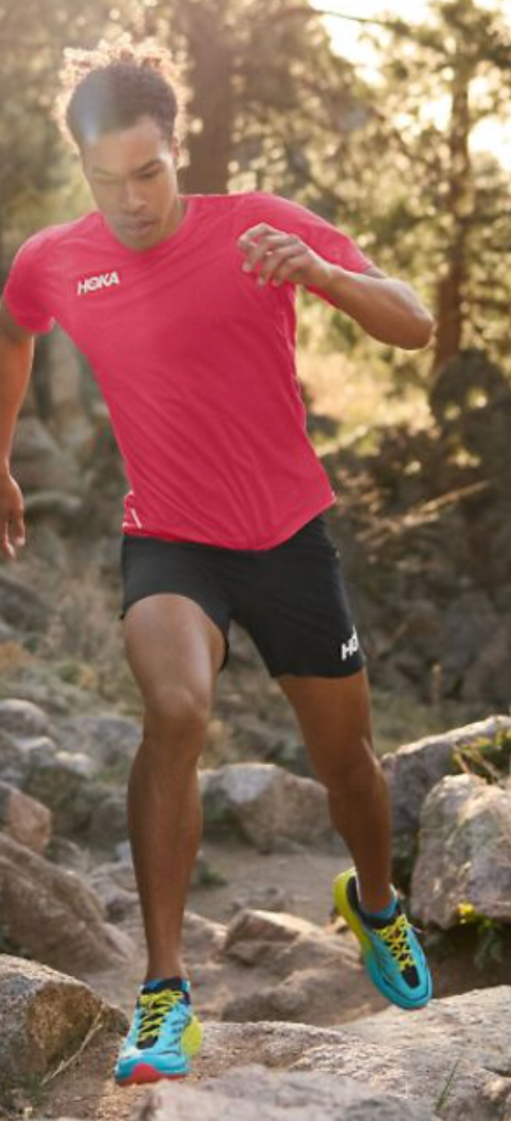 A man running in a Hoka One One outfit with a red shirt, black shorts and colorful sneakers