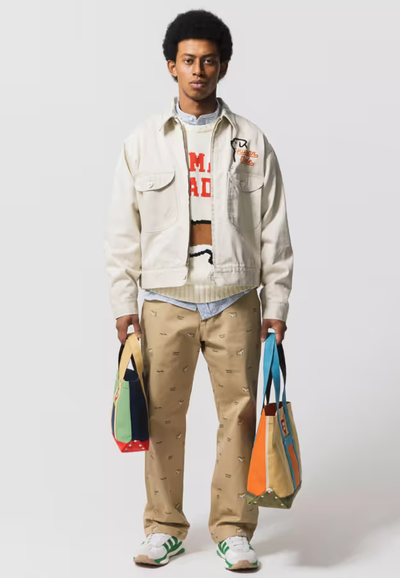 A man wearing a layered Human Made outfit featuring a cream jacket and brown patterned pants