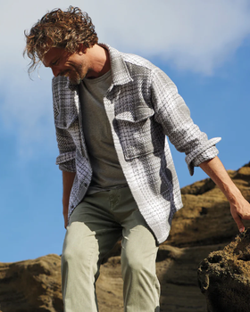 A man climbing outdoors wearing a Outerknown plaid overshirt with light green pants