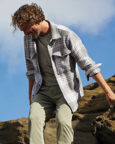 A man climbing outdoors wearing a Outerknown plaid overshirt with light green pants