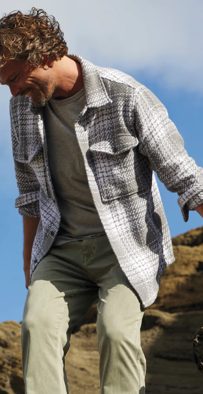 A man climbing outdoors wearing a Outerknown plaid overshirt with light green pants