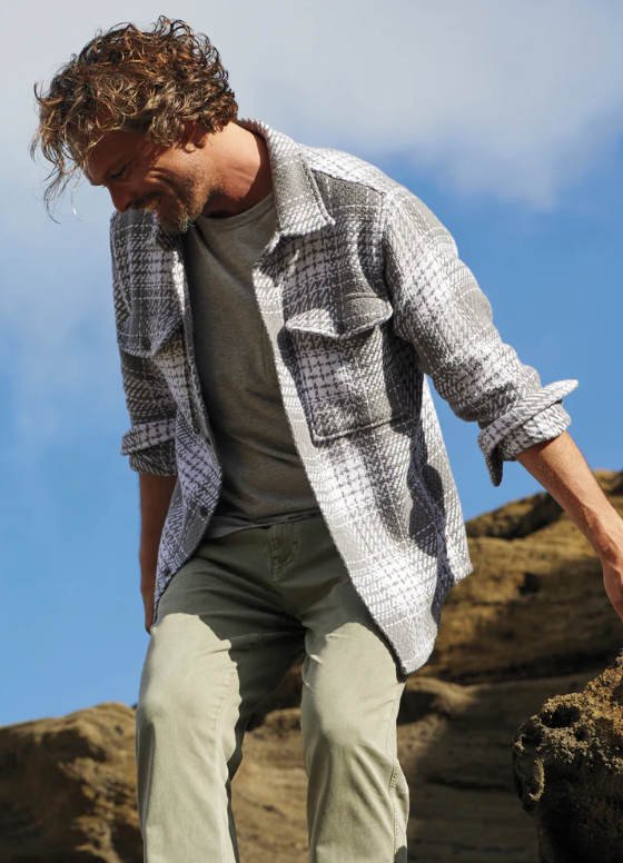 A man climbing outdoors wearing a Outerknown plaid overshirt with light green pants