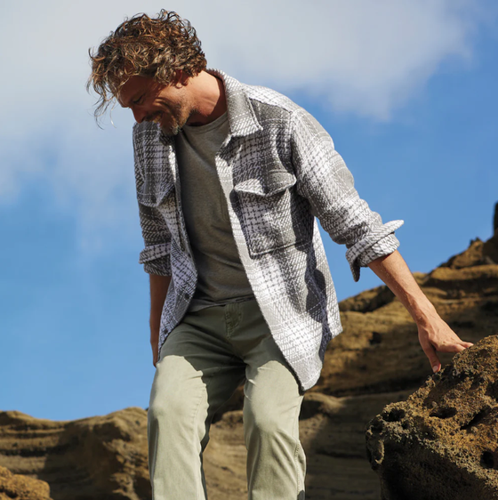 A man climbing outdoors wearing a Outerknown plaid overshirt with light green pants