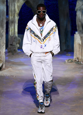 A man wearing a white Versace tracksuit with colorful print and matching sneakers