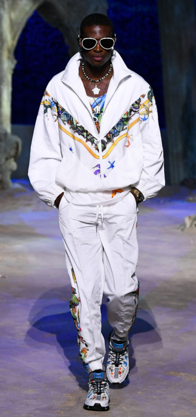 A man wearing a white Versace tracksuit with colorful print and matching sneakers