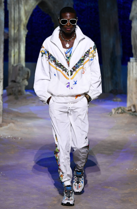 A man wearing a white Versace tracksuit with colorful print and matching sneakers