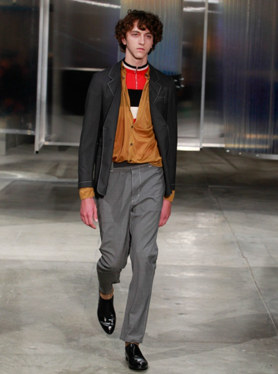 A man wearing a Prada outfit with grey pants and a brown cardigan