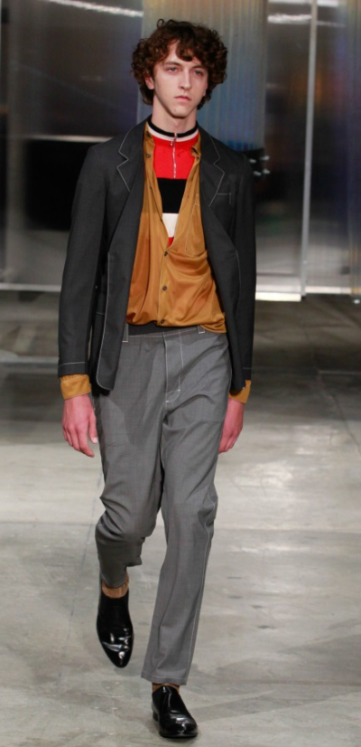 A man wearing a Prada outfit with grey pants and a brown cardigan