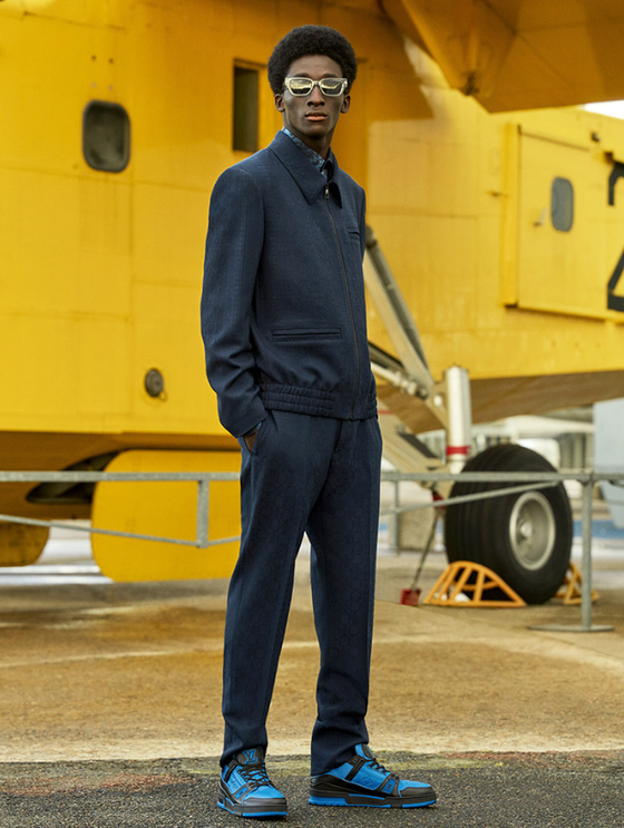 A man wearing a slick Louis Vuitton suit with blue high-top sneakers and gold sunglasses
