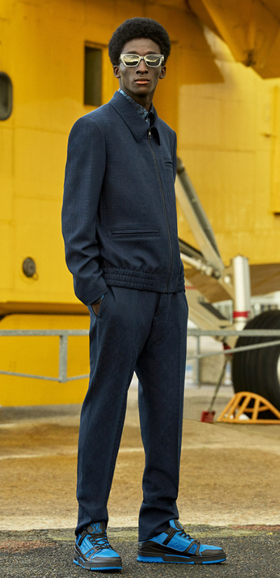 A man wearing a slick Louis Vuitton suit with blue high-top sneakers and gold sunglasses