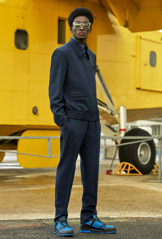A man wearing a slick Louis Vuitton suit with blue high-top sneakers and gold sunglasses