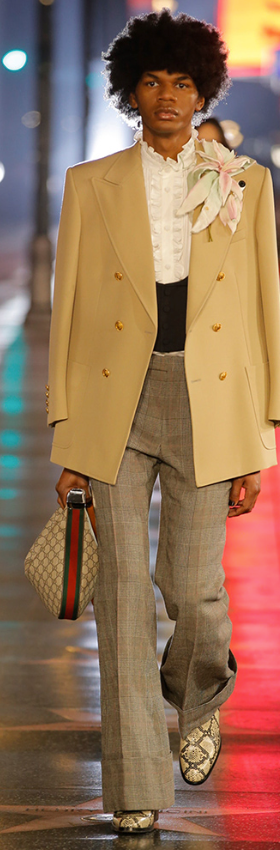 A man wearing a Gucci brown coat and checkered pants with snake skin boots