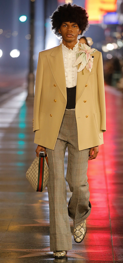 A man wearing a Gucci brown coat and checkered pants with snake skin boots