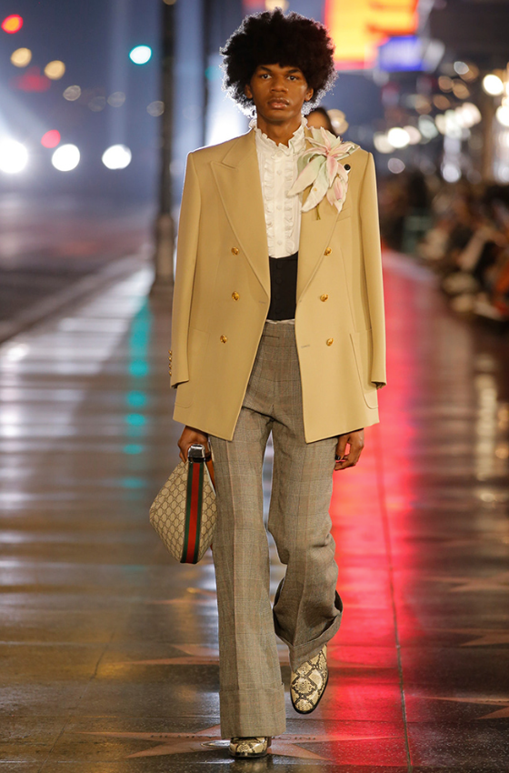 A man wearing a Gucci brown coat and checkered pants with snake skin boots
