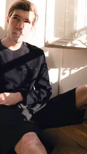 A man sitting in the sun wearing a Magenta Skateboards long-sleeve and shorts