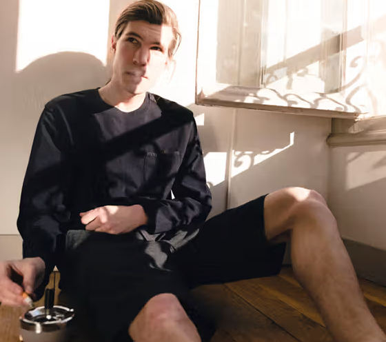 A man sitting in the sun wearing a Magenta Skateboards long-sleeve and shorts