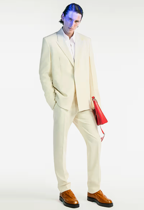 A man wearing a cream Givenchy suit with a red bag and brown shoes