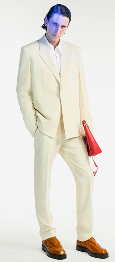 A man wearing a cream Givenchy suit with a red bag and brown shoes