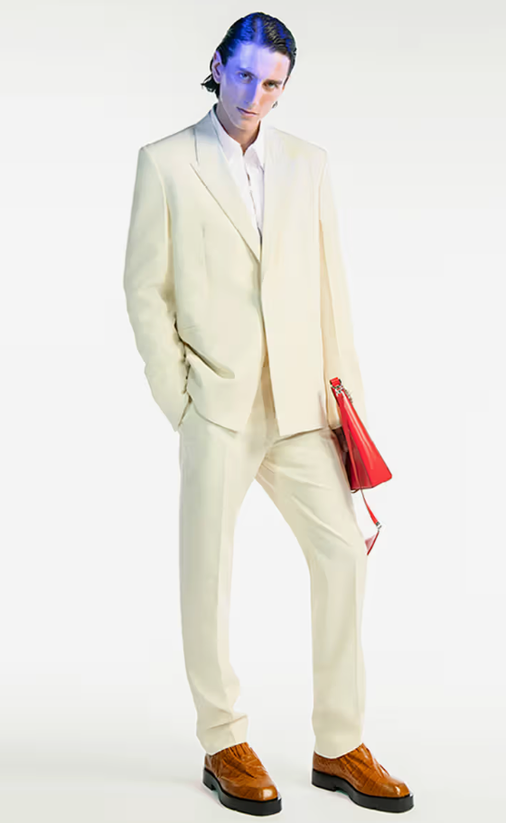 A man wearing a cream Givenchy suit with a red bag and brown shoes