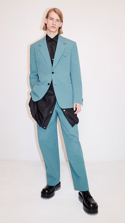 A man wearing a aqua blue suit with a blue jacket underneath along with black loafers