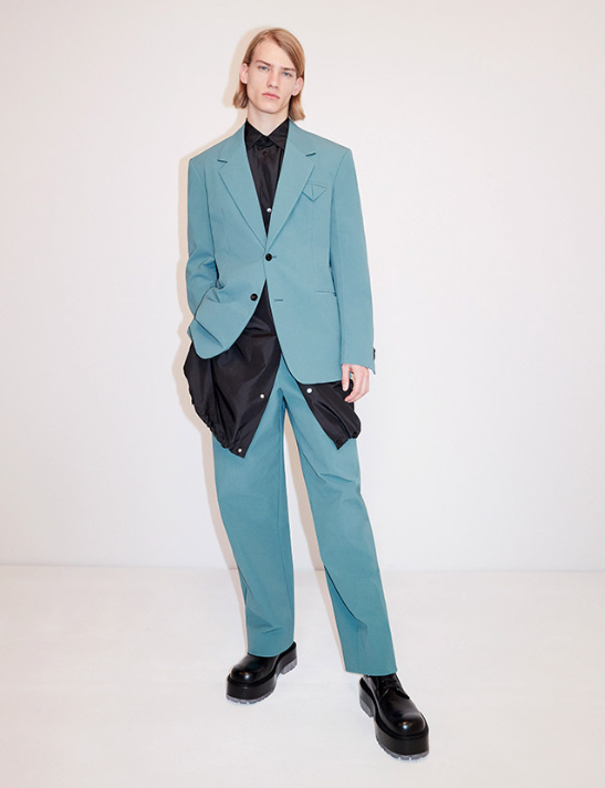 A man wearing a aqua blue suit with a blue jacket underneath along with black loafers