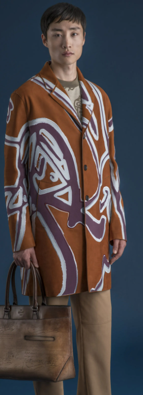 A man wearing a long Berluti jacket with a large purple pattern on top and brown pants