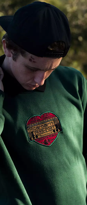 A close up of a man wearing a green Passport Skateboards hoodie with a red heart on it