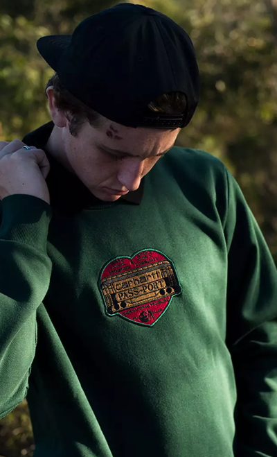 A close up of a man wearing a green Passport Skateboards hoodie with a red heart on it