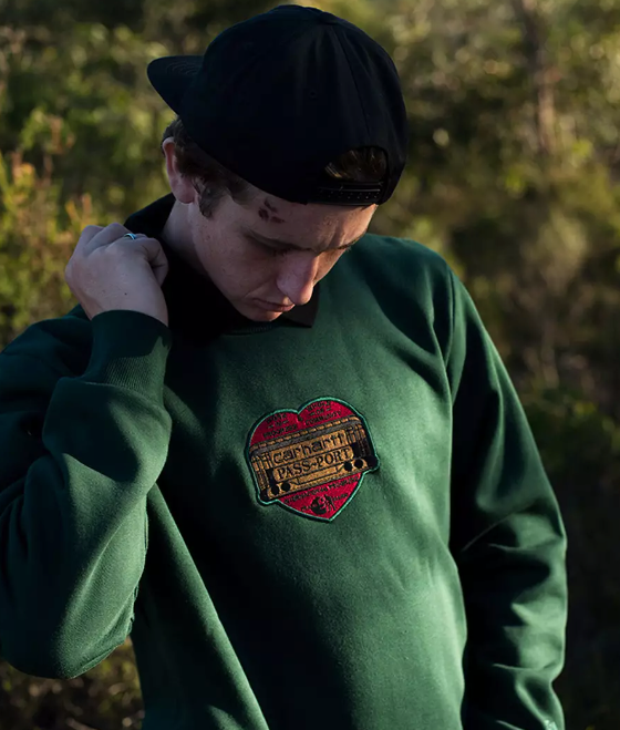 A close up of a man wearing a green Passport Skateboards hoodie with a red heart on it