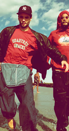 Two men walking on the beach wearing red QuarterSnacks Sweatshirts and baggy pants