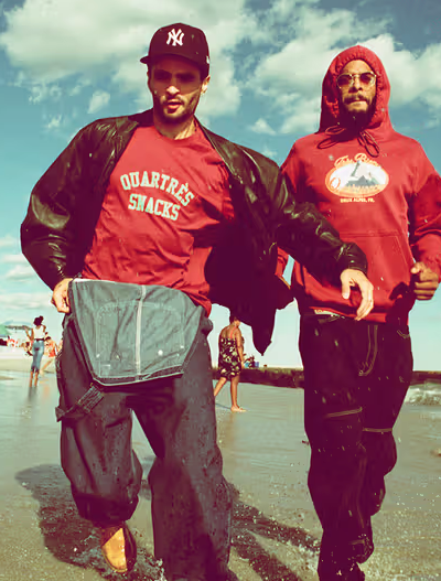 Two men walking on the beach wearing red QuarterSnacks Sweatshirts and baggy pants