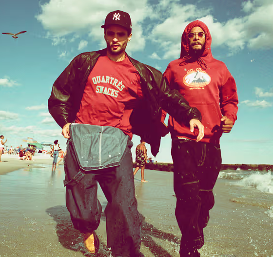 Two men walking on the beach wearing red QuarterSnacks Sweatshirts and baggy pants