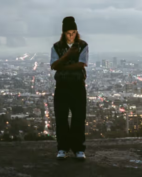 A man standing on a mountain above the city wearing a Polar Skate Co. Sweater and Pants