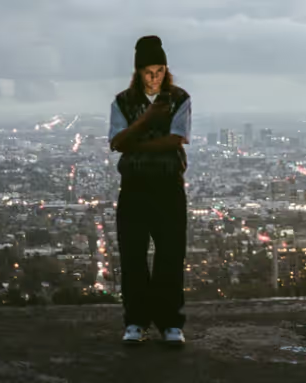 A man standing on a mountain above the city wearing a Polar Skate Co. Sweater and Pants