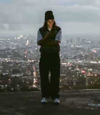 A man standing on a mountain above the city wearing a Polar Skate Co. Sweater and Pants