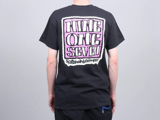 A man wearing a Call Me 917 t-shirt with a large print on the back in pink and white