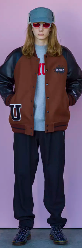 A man wearing an Undercover outfit featuring a coaches jacket, sweatshirt, black pants and snakeskin boots