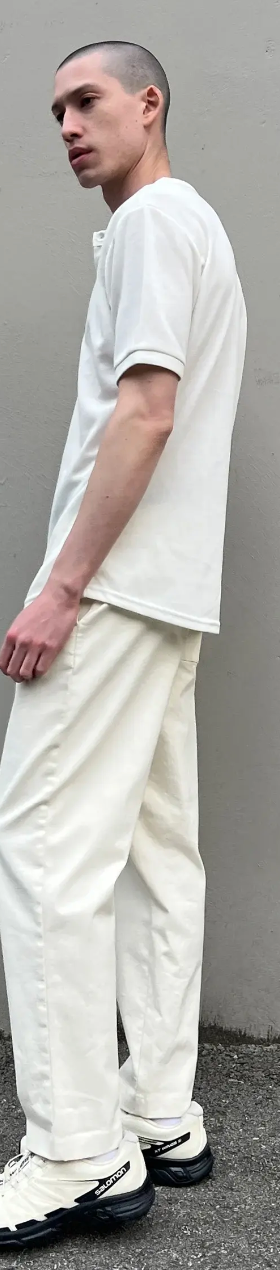 A man standing outside wearing a Oak + Fort all-white and cream outfit with salomon shoes
