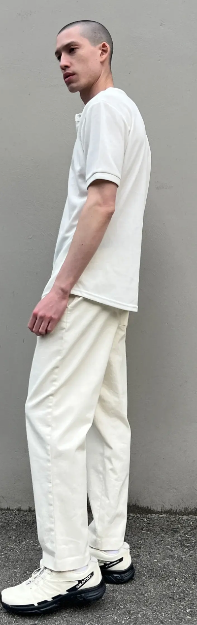 A man standing outside wearing a Oak + Fort all-white and cream outfit with salomon shoes