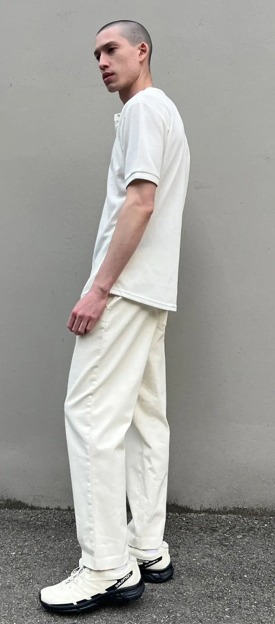 A man standing outside wearing a Oak + Fort all-white and cream outfit with salomon shoes
